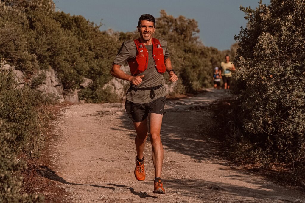 Smiling man jogging on a sunny trail, capturing the essence of outdoor fitness and healthy lifestyle.